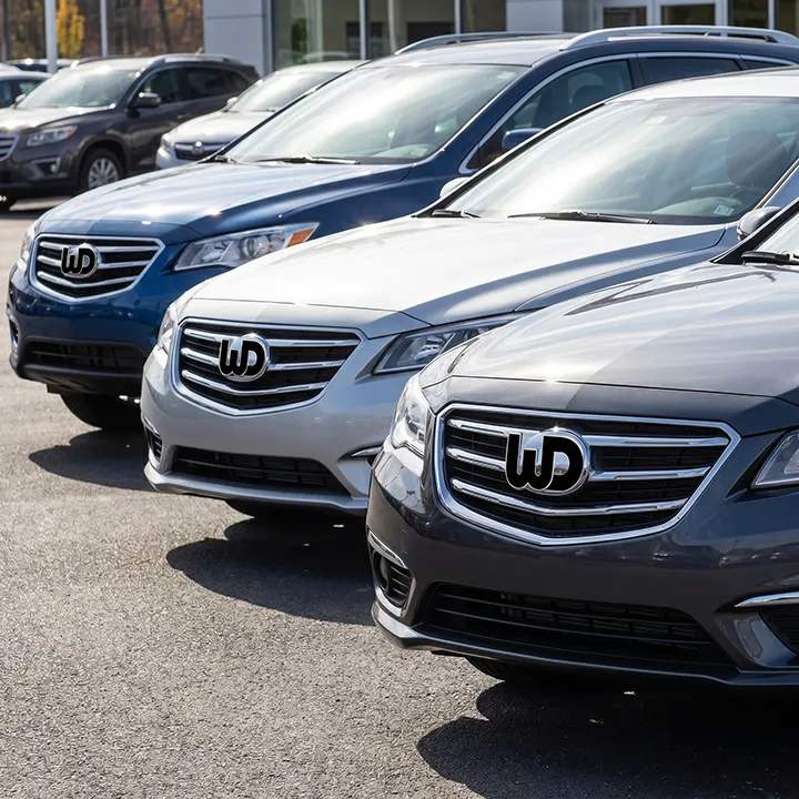 Row of modern sedans in a lot with the Womp Designs logo on their front grilles.