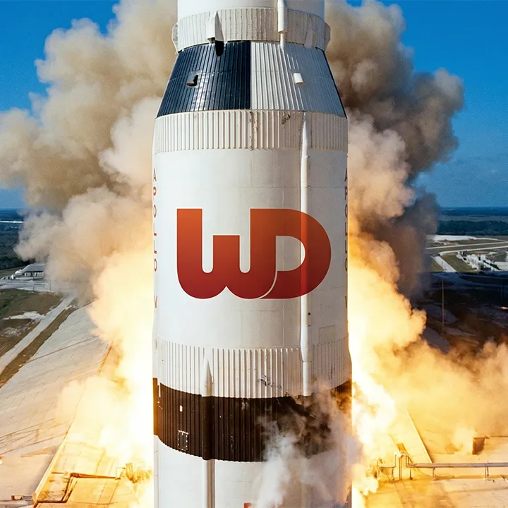 Saturn V rocket launching with a large orange-to-red gradient Womp Designs logo on its side.