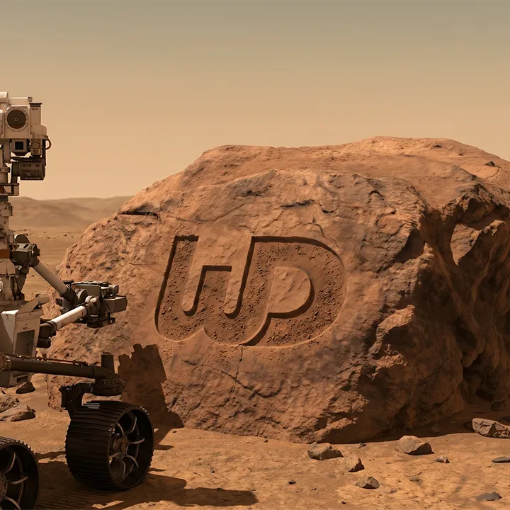 Mars rover next to a reddish boulder with a Womp Designs logo carved into the rock.